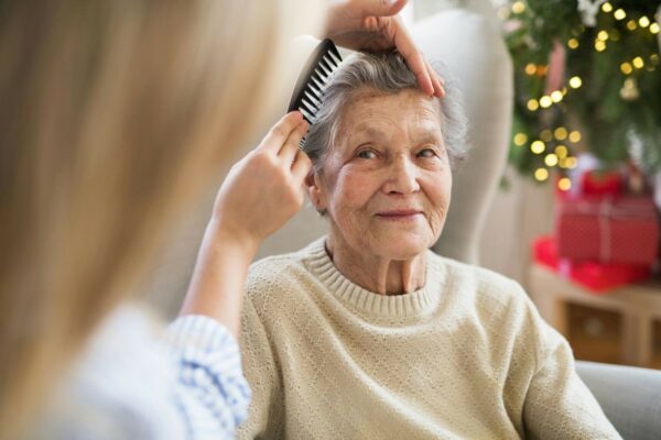 Caregiver helping to old woman to comb her hair