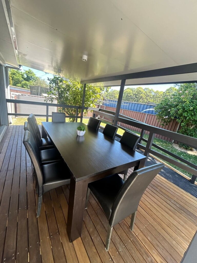 An outdoor dining area on a wooden deck with a table set for six under a covered patio, ideal for supported independent living in Lethbridge Park NSW.