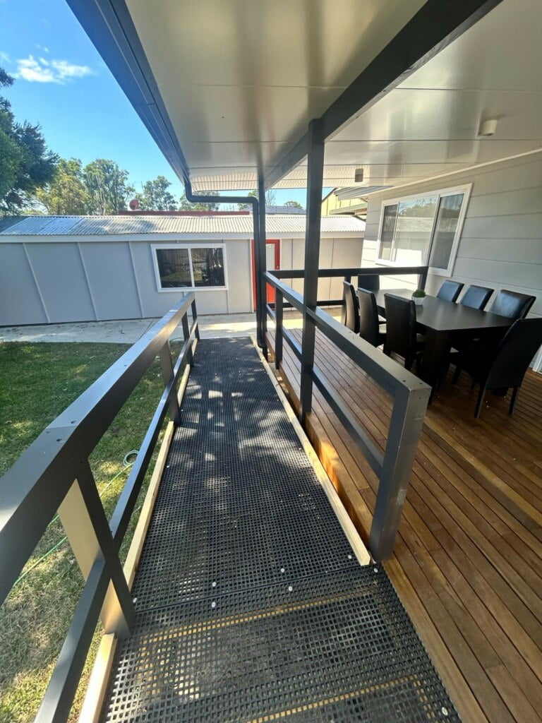 An outdoor residential patio with metal grate flooring and a dining set in the background, shaded by an overhanging roof, offers a perfect setup for independent living in Lethbridge Park NSW.