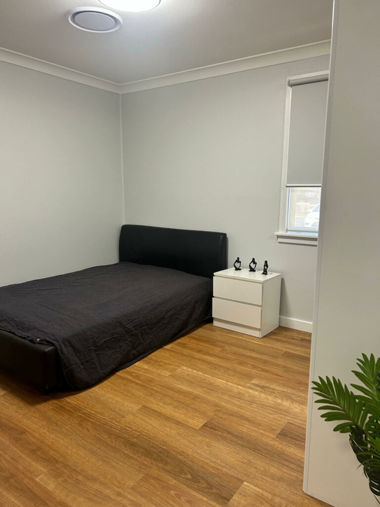 A minimalistic bedroom in Lethbridge Park NSW with a single bed, a small bedside table, and a potted plant, designed for supported independent living.