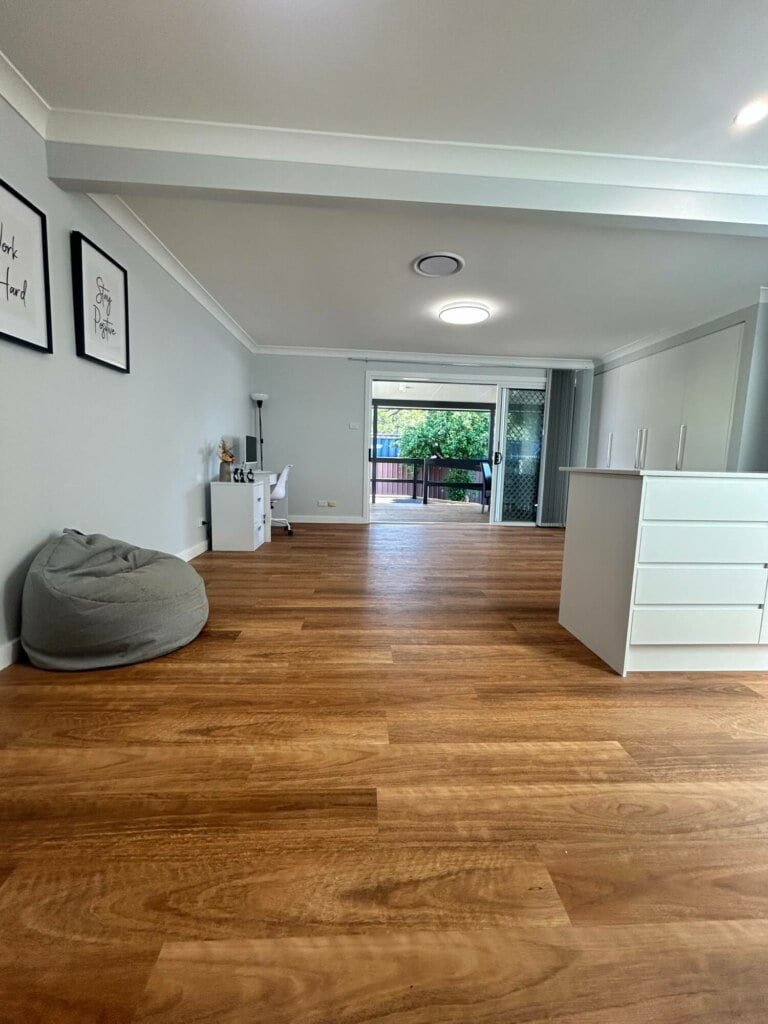 A clean, modern room with wooden flooring, white furniture, and wall art leading to a balcony, perfect for supported independent living in Lethbridge Park NSW.