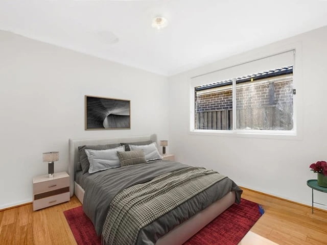 A neatly presented bedroom in SIL Home Ropes Crossing with a double bed, grey bedding, a white side table, and a red area rug.