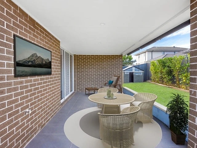 Covered patio area with wicker furniture and a lawn view, adjacent to a brick house in Sydney.