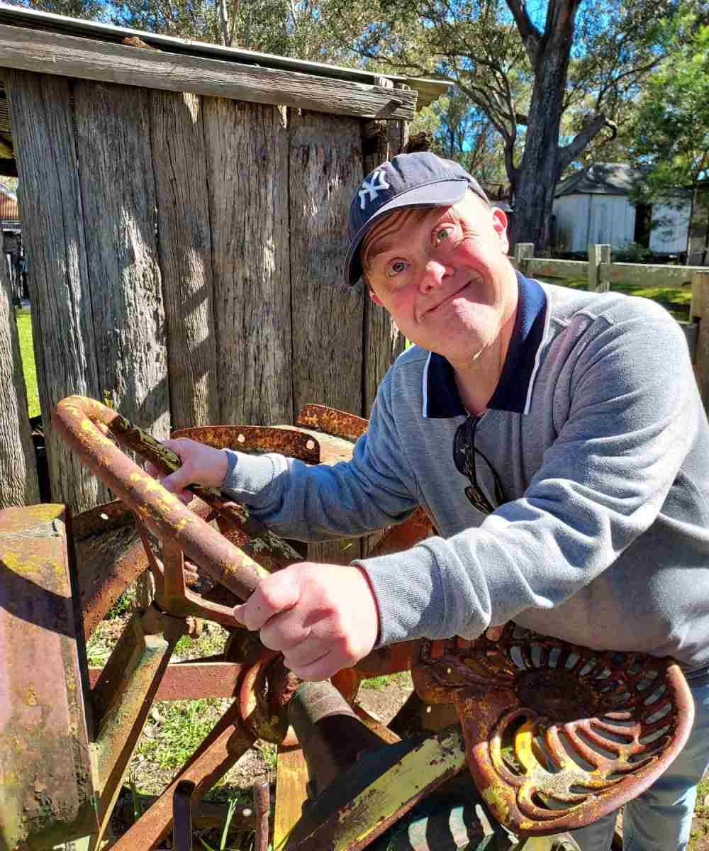 A man in a hat is standing next to a rusty old tractor.