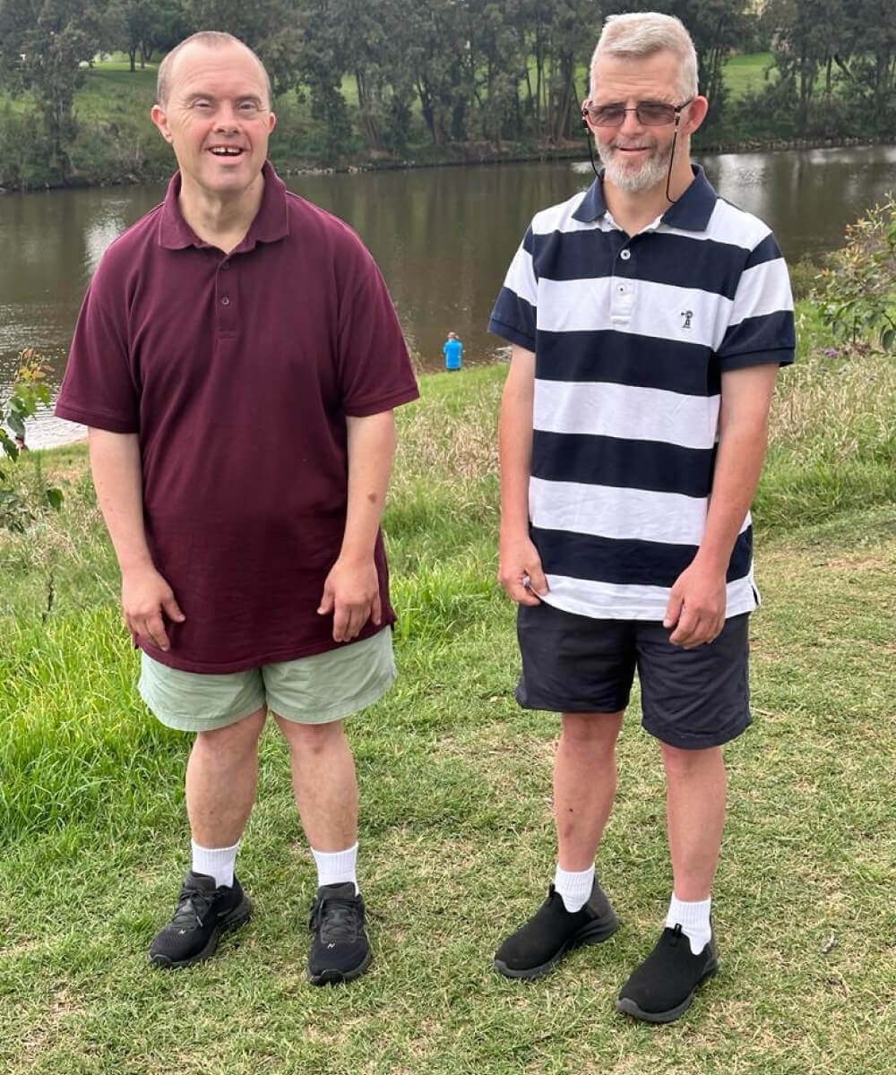 Two men standing next to each other in front of a river.